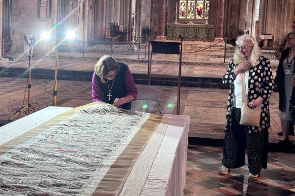 Bishop Debbie placing final stitches in embroidery of Peterborough Cathedral ceiling