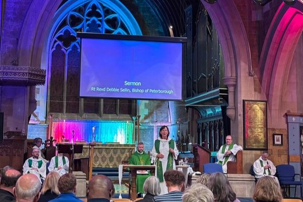 Bishop Debbie preaching the sermon from the front of St Andrew's Church and Arts Centre, Kettering. Coloured lighting in blue, pink and purple illuminate